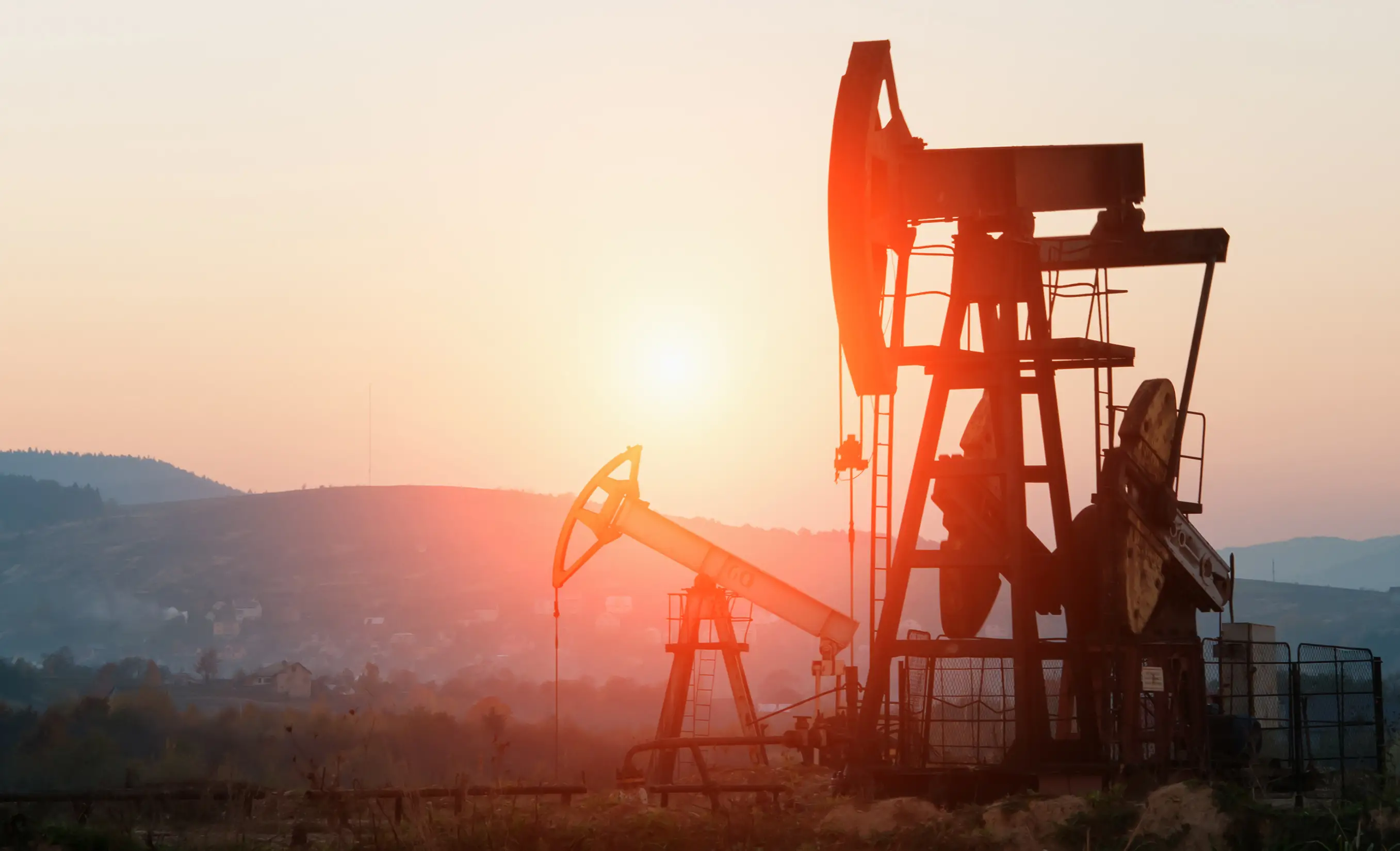 A sunset over an oil well with the sun setting.